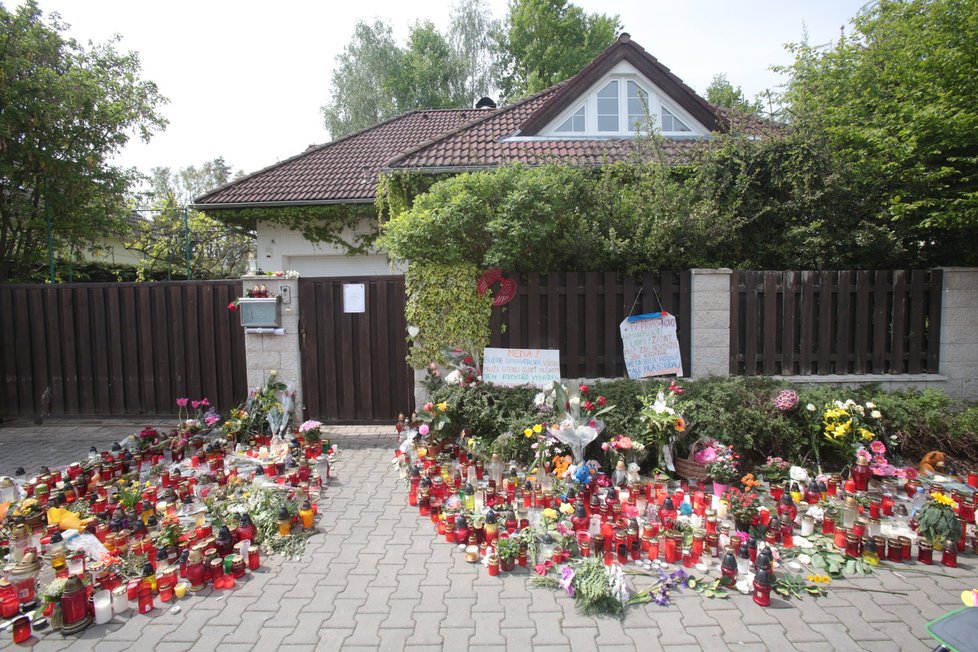 Mezitím se ulice před vchodem do domu Bartošové zaplňuje svíčkami a květinami.