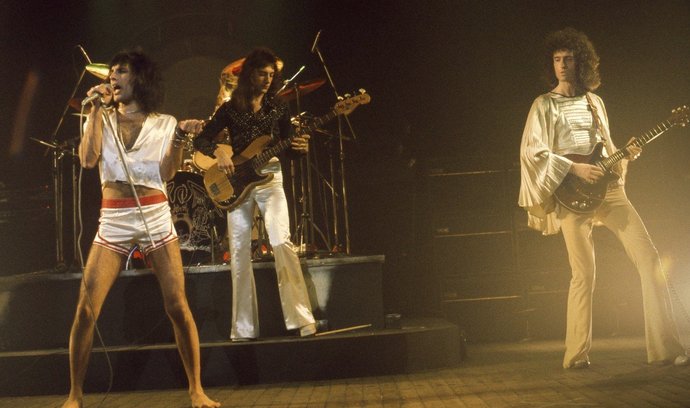 Kapela Queen. Freddie Mercury u mikrofonu, po jeho levici vlasáč Brian May. Jeho odhadované jmění je 210 milionů dolarů.