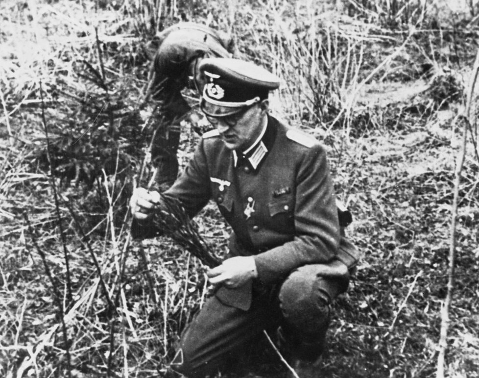 Německý důstojník prohledává okolí masových hrobů.