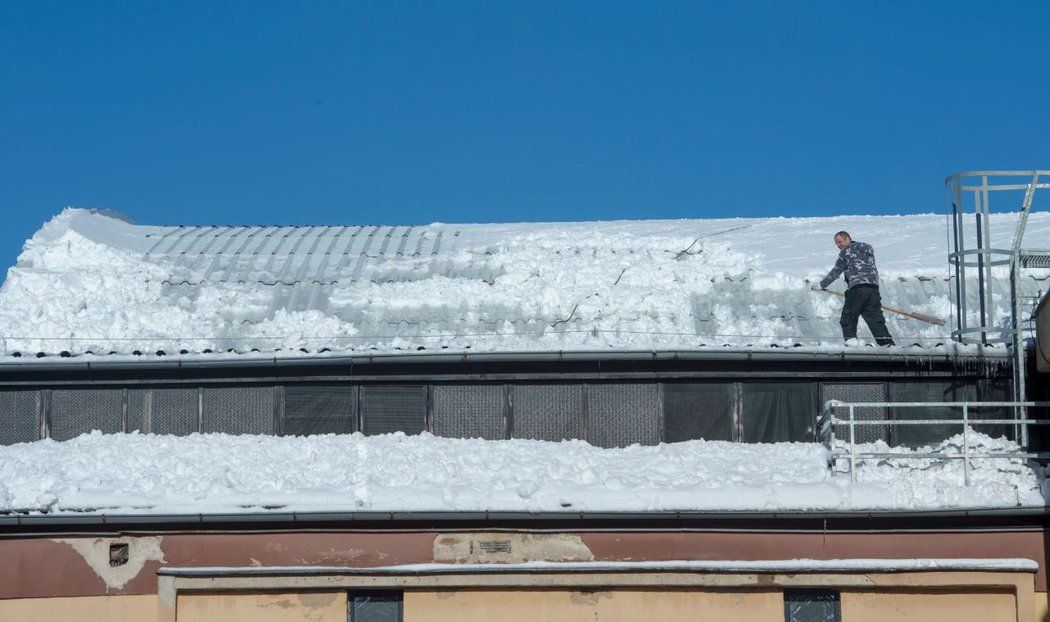 Horolezec odstraňuje návaly sněhu, které dostaly pod drtivý nápor stařičkou střechu kladenského zimáku