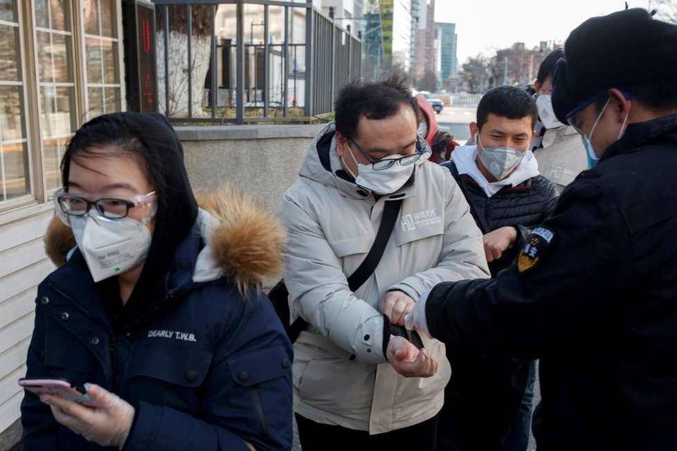 Pracovník měří teplotu lidem na cestě do práce v Pekingu (3.3.2020)