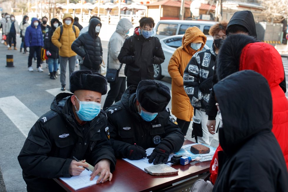 Pracovník měří teplotu lidem na cestě do práce v Pekingu (3.3.2020).