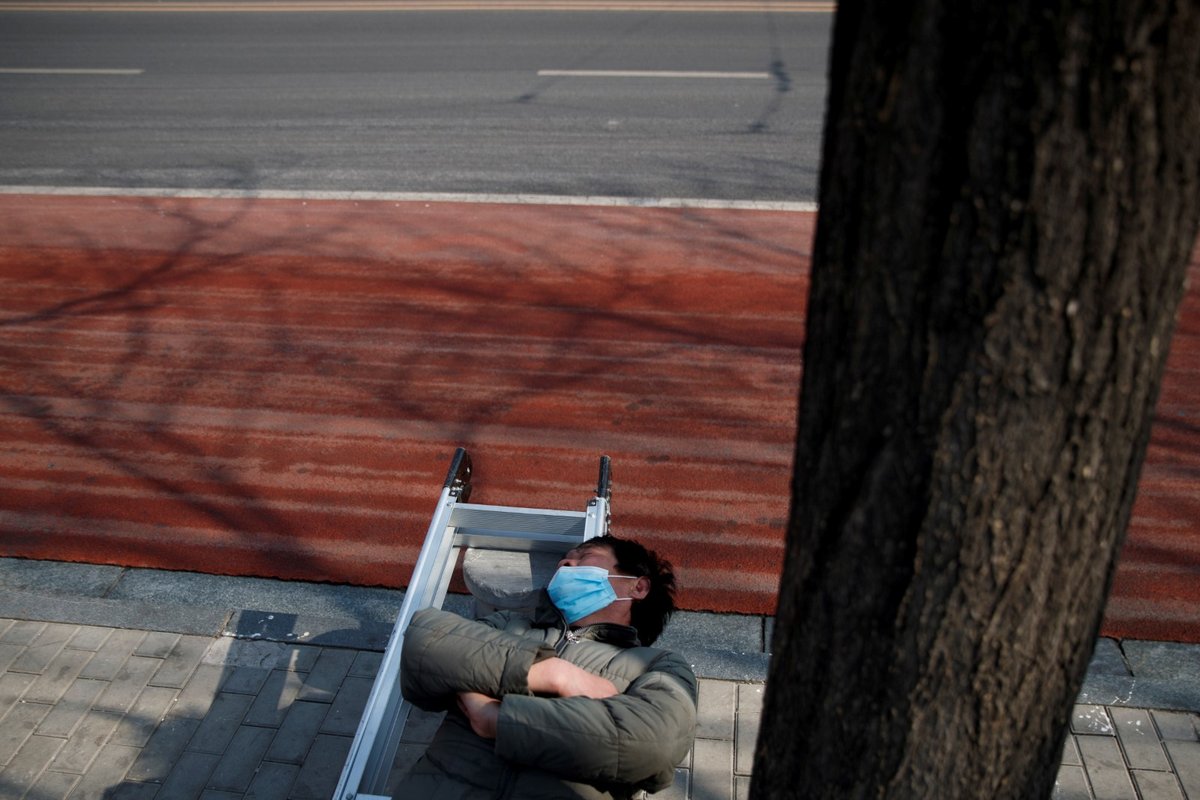 Muž spící v ochranné roušce na lavičce v Pekingu