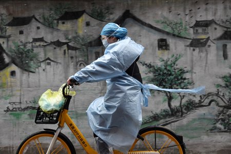 Žena na kole v obytné čtvrti ve Wu-chanu, odkud koronavirová nákaza přišla