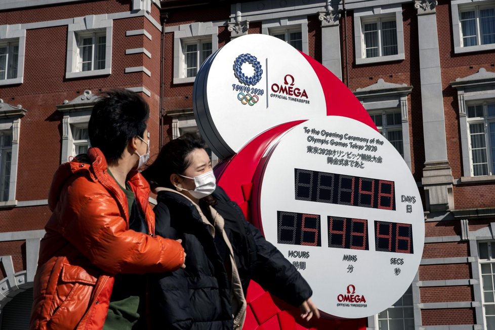 Lidé v rouškách stojící před hodinami, které odpočítávají čas do zahájení Olympijských her v Tokiu 2020 (27.2.2020)