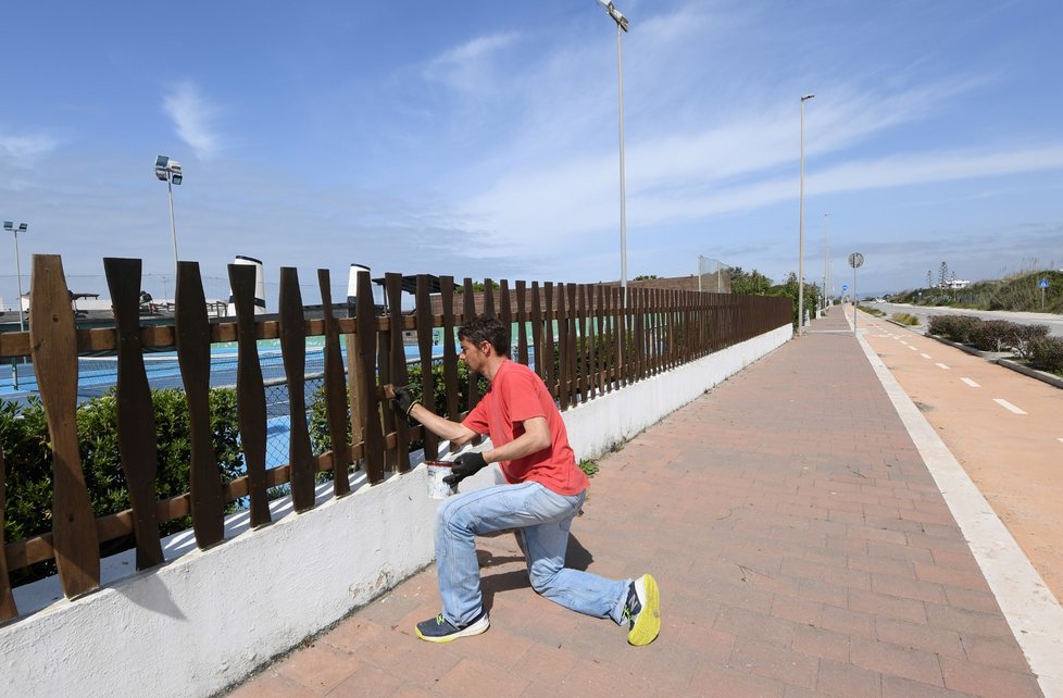 Muž maluje plot před zavřeným plážovým resortem v Itálii. (18. 4. 2020)