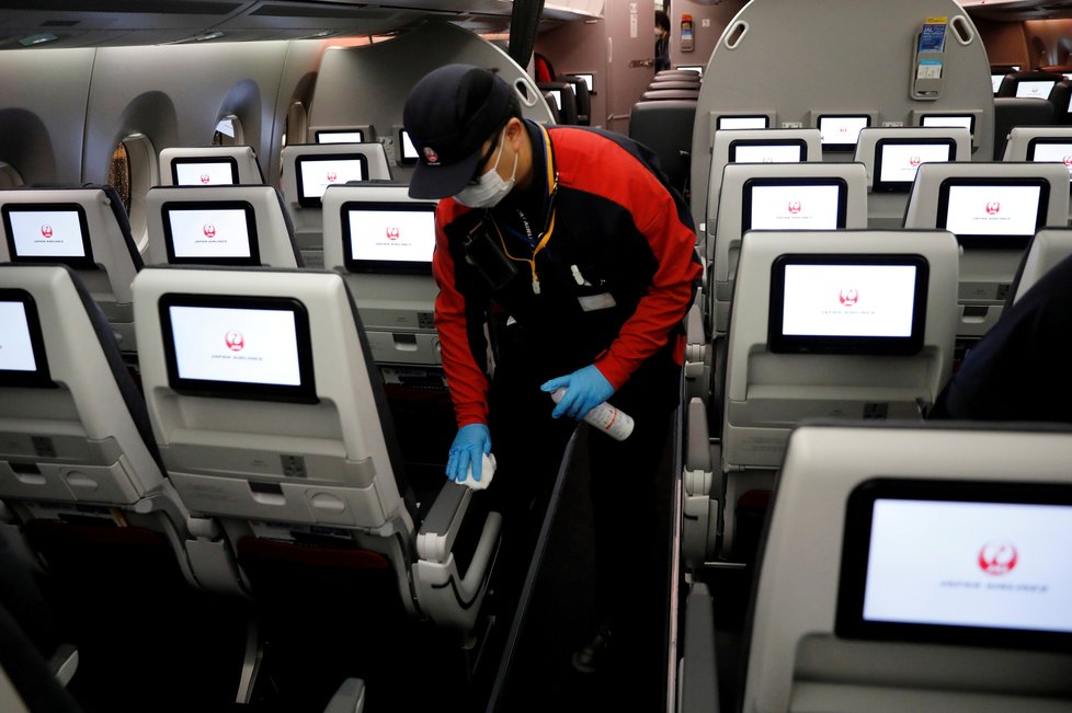 Zaměstnanci aerolinek Japan Airlines po první letu po obnovení vnitrostátní letecké dopravy dezinfikují letadlo, (26.05.2020).