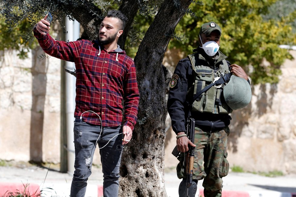 Muž si fotí selfie s členem palestinských bezpečnostních jednotek s ochrannou maskou (5.3.2020)