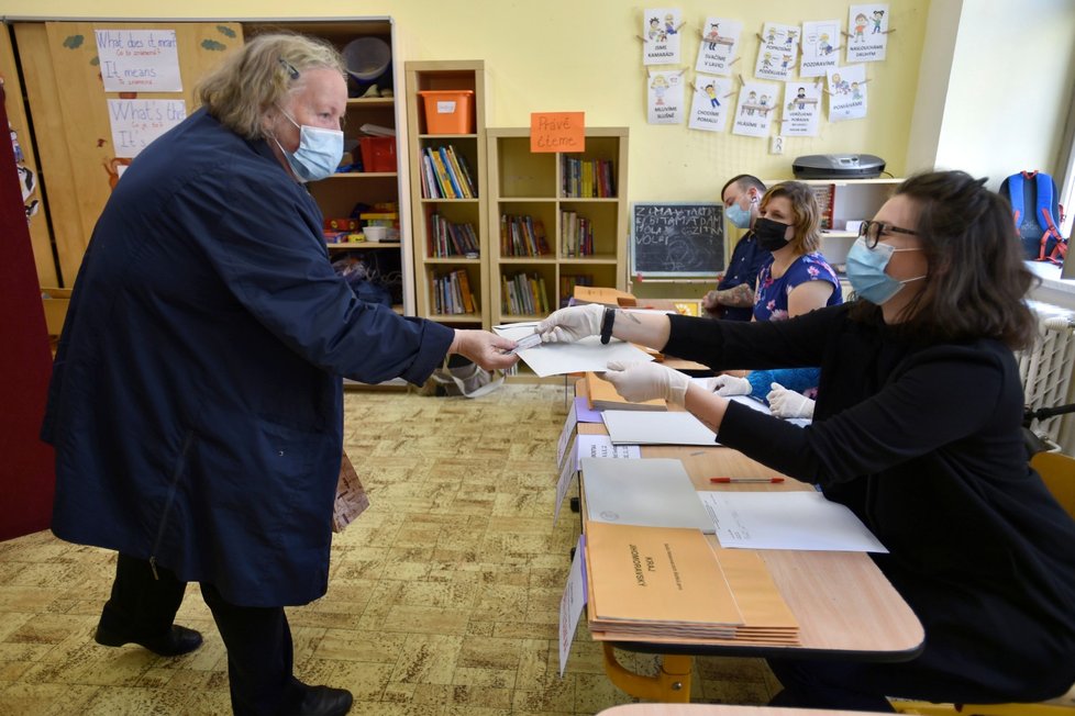 Členka volební komise předává voličce po ověření totožnosti obálku na hlasovací lístky v budově základní školy v Rašínově ulici v Brně (2. 10. 2020)