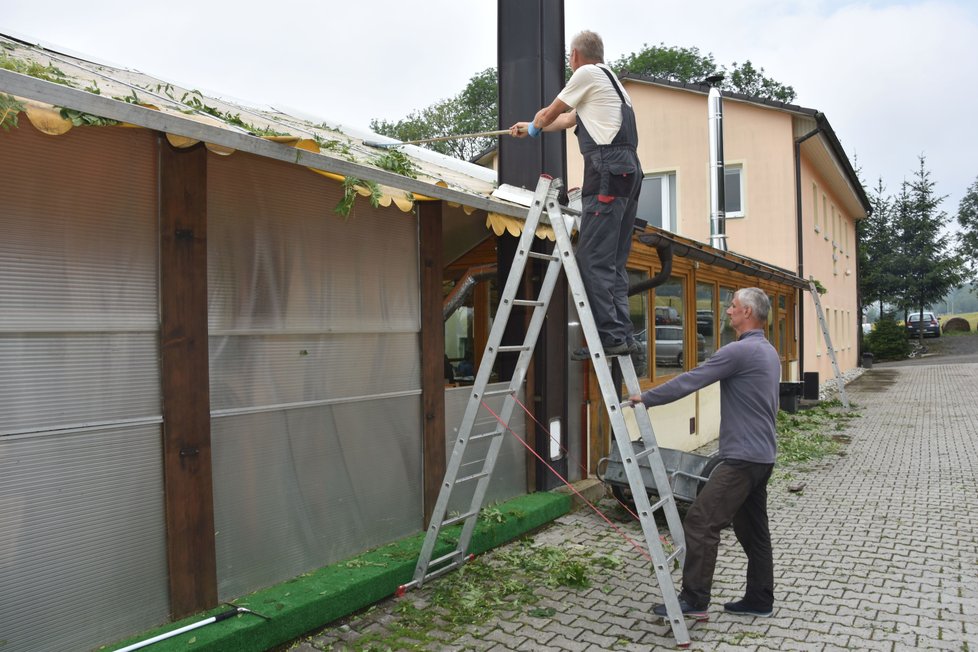 Lidé shrabují z rozbité střechy restaurace větve a listí.