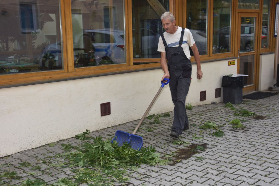 Lidé uklízejí před restaurací úlomky větví a listí.