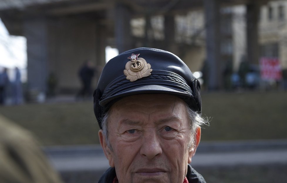 Muž stojí před budovou parlamentu v Simferopolu. Na hlavě má čepici s emblémem sovětského námořnictva.