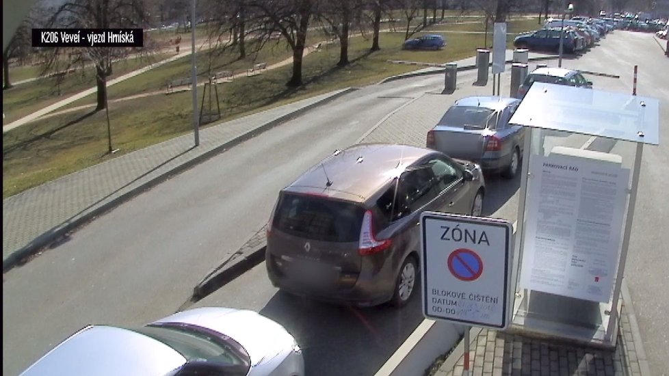 Pohled z jiné kamery: ...auto míří do parku mezi stromy, žena jej marně stíhá...