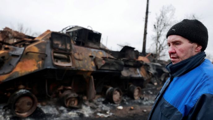Vedle zničeného vojenského vozidla v Buče stojí místní obyvatel.