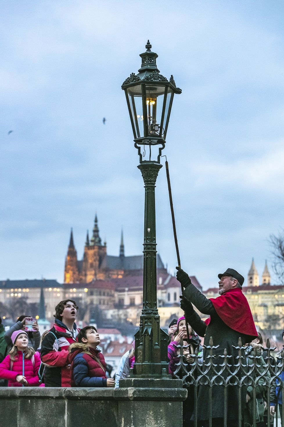 Každoroční adventní atrakce na Karlově mostě. Lampář Jan Žákovec ručně, tudíž postaru, rozsvěcuje plynové lampy. Lecjakému turistovi přitom zůstává pusa dokořán.