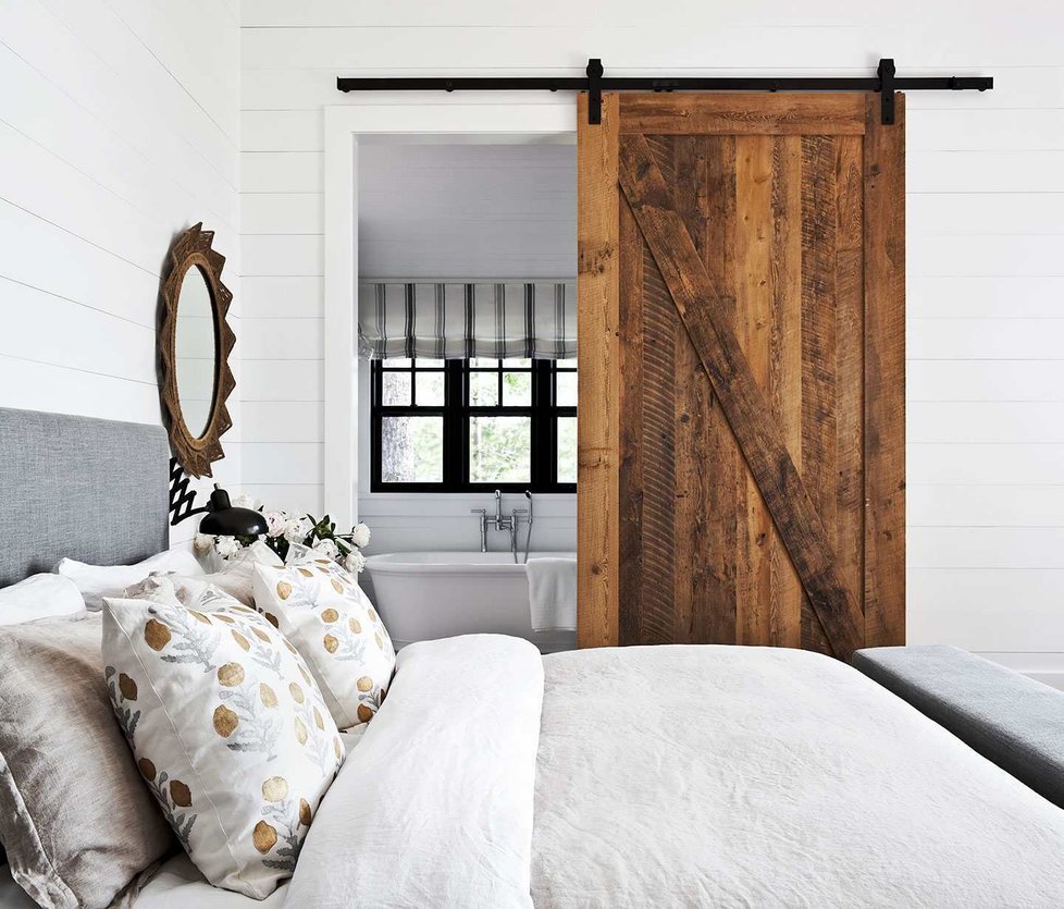 Moderně zařízené ložnici dodávají kouzlo venkovsky laděné doplňky v podobě rámu zrcadla, natahovací nástěnné lampičky z kovu a nádherných posuvných dveří z masivu.