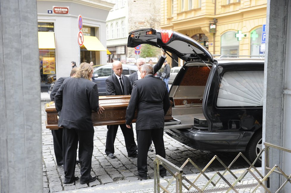 Pracovníci pohřební služby nakládají rakev zpět do pohřebního vozu.