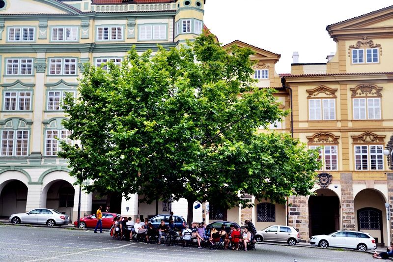 Malostranské náměstí je oázou klidu. Auta už jsou konečně pryč, těší se lidé vysedávající pod stromy.