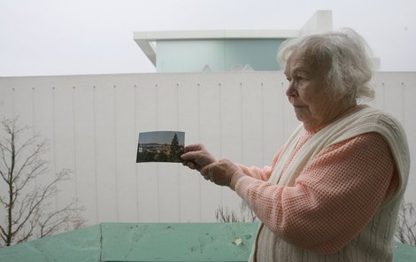 Marie Perlíková ukazuje, co ještě nedávno mohla z balkonu sledovat. Teď už jí zbývá jen pohled na bílou zeď.