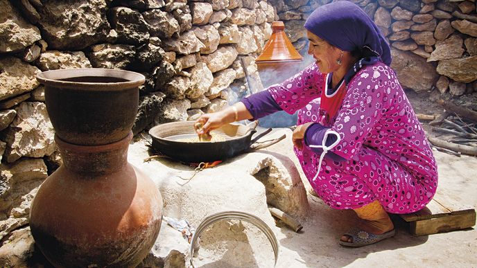 Berberská žena praží podrcená zrna na kuskus na ohni a míchá vše zvířecí lopatkovou kostí