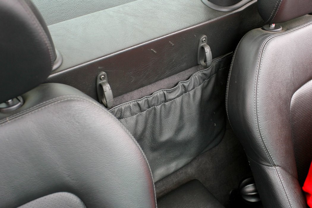Koženková kapsa mezi opěradly sedadel pojme klidně i velký autoatlas, gumička však má sklony k nevzhlednému vytahání