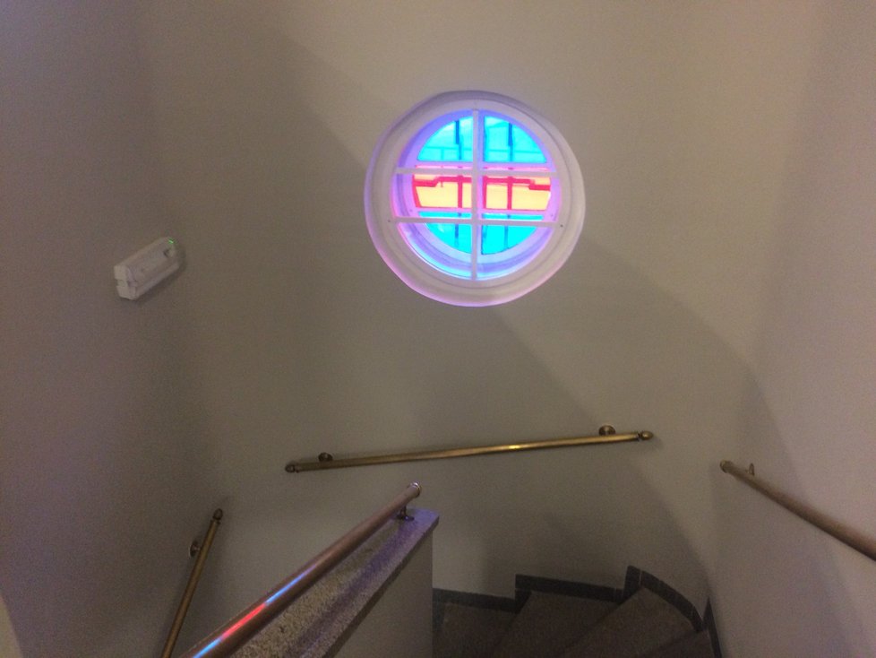 Barevné kulaté okno podle achitekta Hořavy ozvlášotnilo jinak šedý úzký prostor schodiště.
