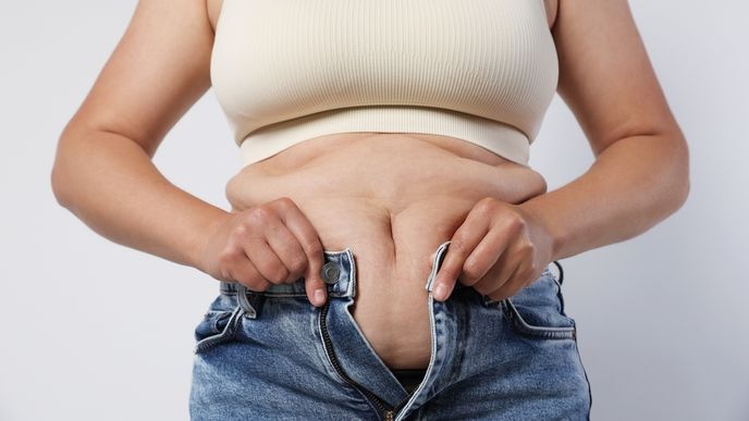 Overweight woman trying to put on tight jeans against light background Overweight woman trying to put on tight jeans against light background