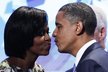 Barack Obama líbá manželku Michelle, šedovlasý pán, který přihlíží v zákrytu, je Bill Clinton