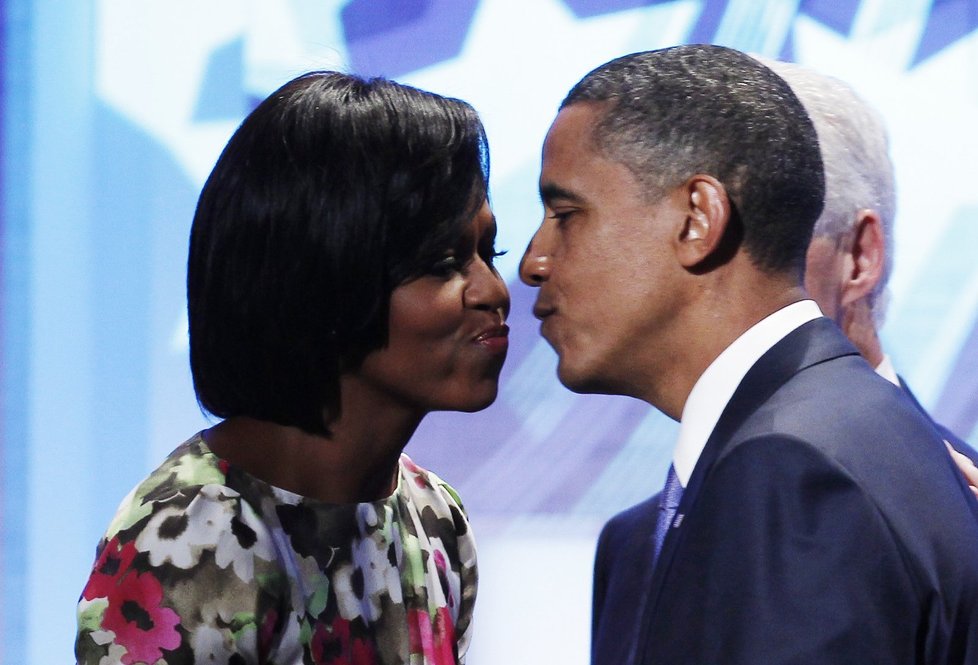 Barack Obama líbá manželku Michelle, šedovlasý pán, který přihlíží v zákrytu, je Bill Clinton