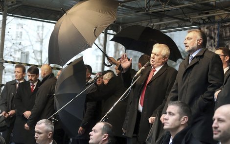 Miloš Zeman musel řečnit, resp. překřikovat dav, ukrytý pod deštníky ochranky.