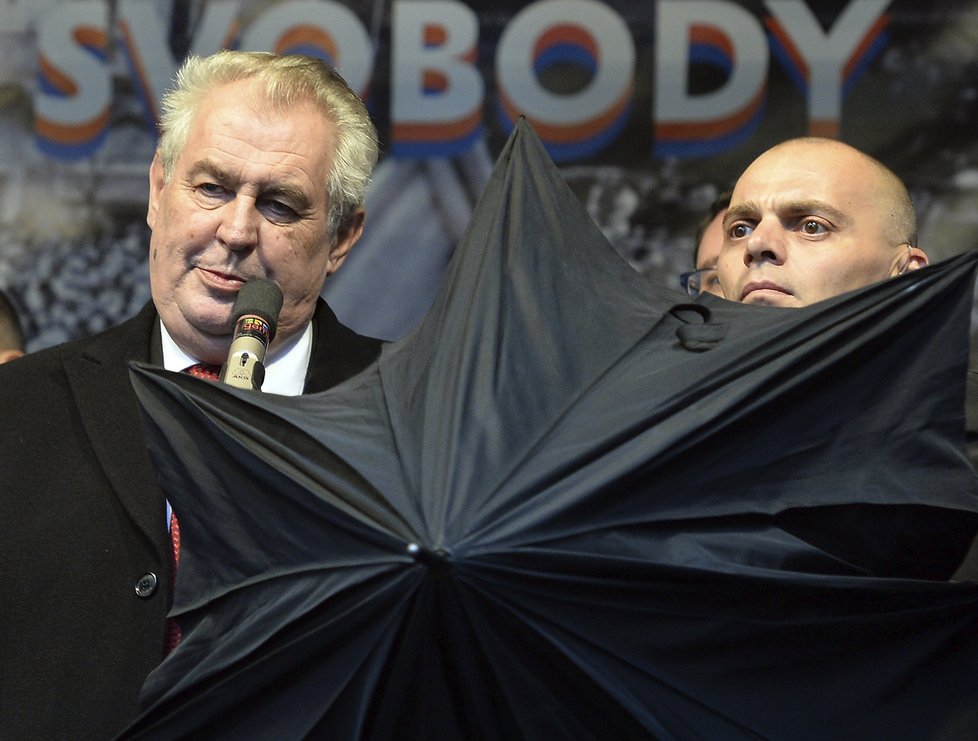 Prezident Zeman na Albertově, kde ho deštníky kryli členové ochranky před rozvášněnými odpůrci