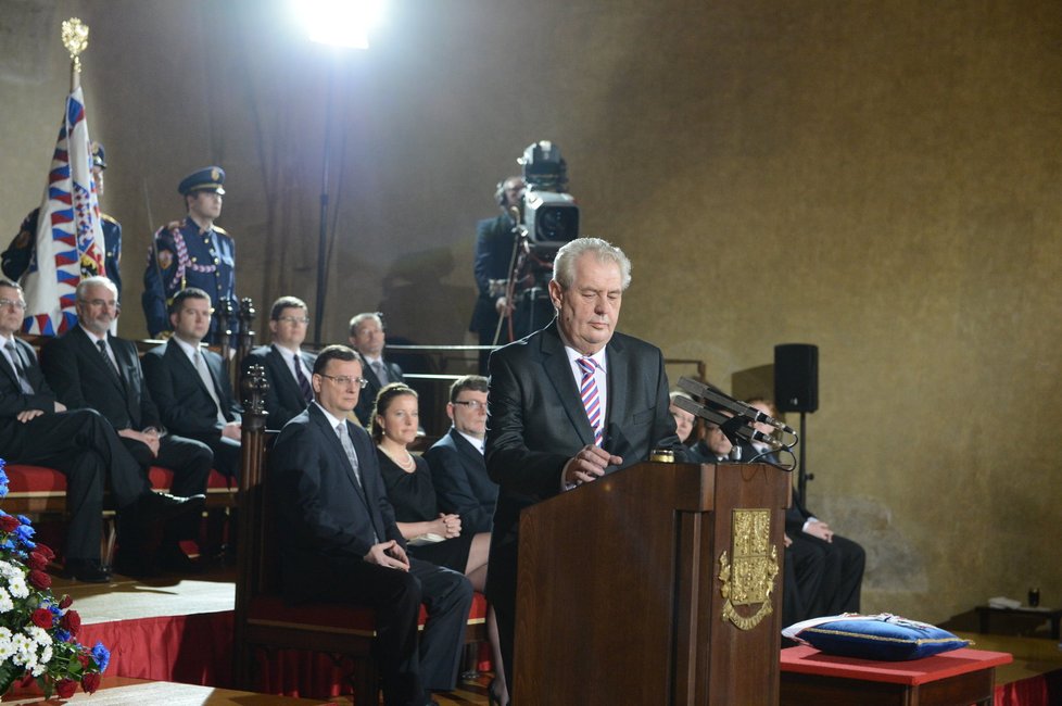 Během čtení prezidentského projevu Miloši Zemanovi vyschlo v krku, a tak musel sáhnout po vodě. Za ním sedí členové vládního kabinetu v čele s premiérem Nečasem a vicepremiérkou Peake.