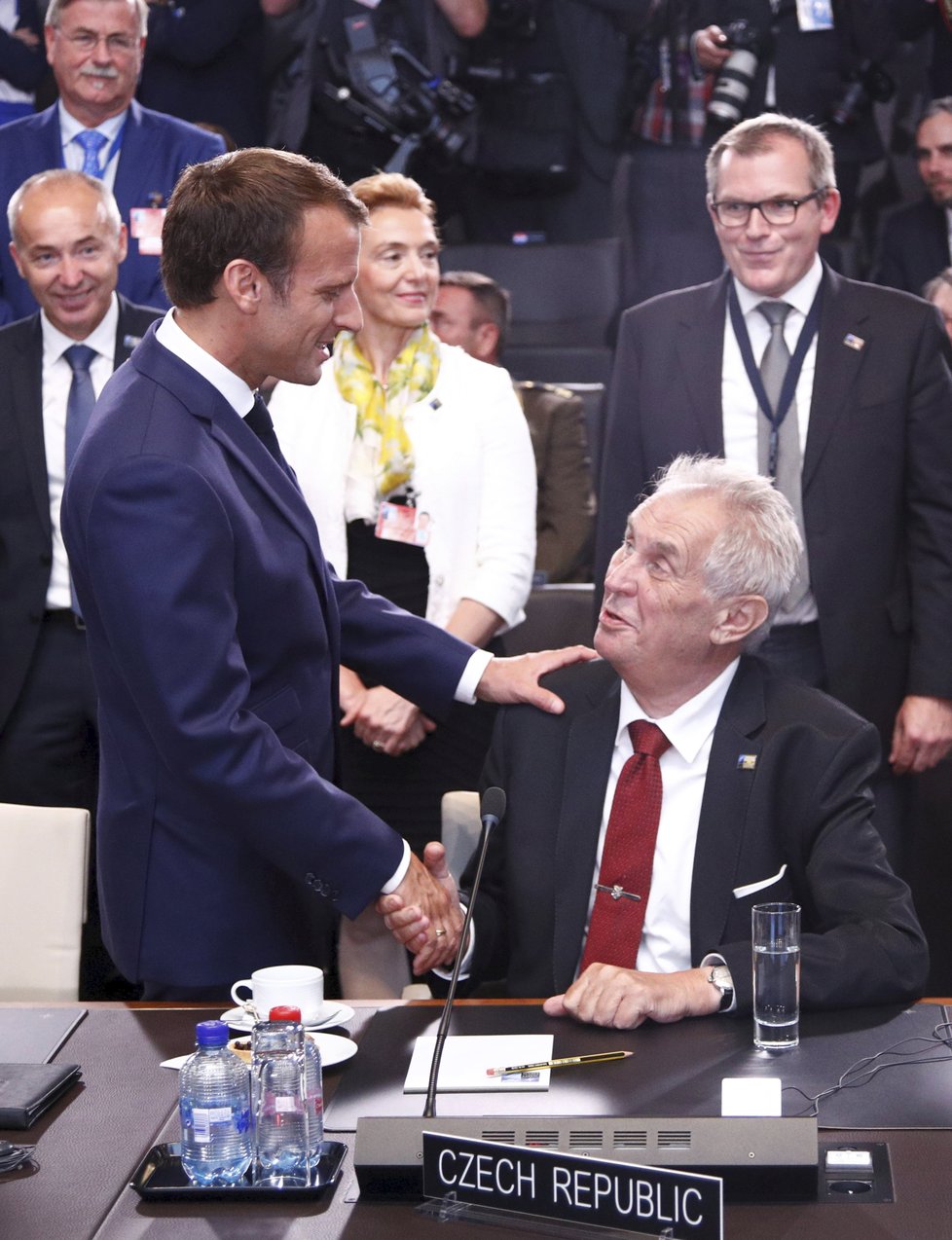 Francouzský prezident Emmanuel Macron zdraví sedícího Miloše Zemana na summitu NATO v Bruselu