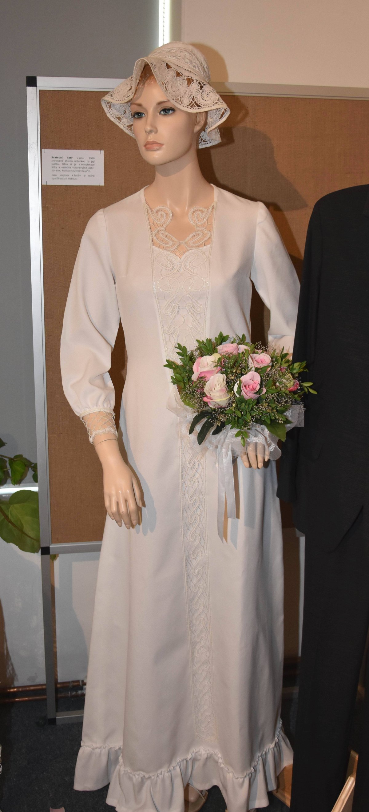 Svatební šaty z roku 1980. Zhotovila si je místní ašská občanka na svou svatbu. Ušila si je z krimplenové látky a ozdobila vlastnoručně paličkovanou krajkou s lurexovou přízí. Jako doplněk k šatům si ručně upaličkovala i klobouk.