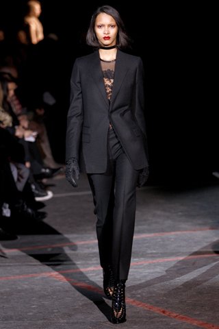 Óda na černou. Strohý kalhotový kostým s cigaretovými kalhotami Krajkový top, šněrovací kotníčkové boty a místo náhrdelníku stužka. Módní dům Givenchy patří k těm, jež rafinovaně propojují pánský styl s žensky působivými detaily.