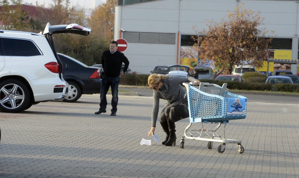 S plnou papírovou taškou zamířila k mercedesu, kde na ni čekal řidič. Nakonec ještě uklidila sfouknutou účtenku a pak i vozíček.