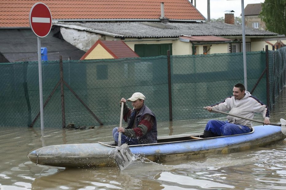 Muži na člunu projíždějí obcí Zálezlice na Mělnicku, kterou zasáhla 4. června povodeň.