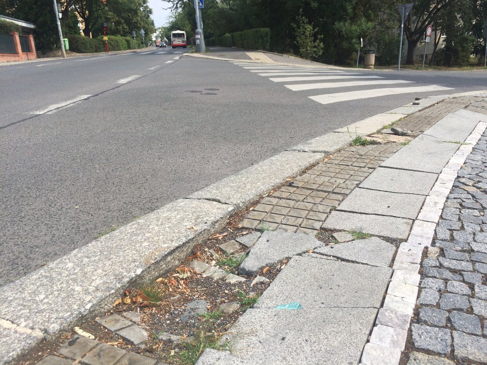 Nároží chodníku na křižovatce ulic Na pískách, Sušická a Vilímovská. Stav je dán nešetrnou jízdou řidičů, kteří přes chodník často přejíždějí.