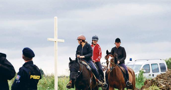 Dívky na koních z nedaleké jízdárny projíždějí kolem čerstvě vztyčeného kříže u hromadného hrobu za Dobronínem