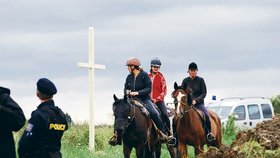 Dívky na koních z nedaleké jízdárny projíždějí kolem čerstvě vztyčeného kříže u hromadného hrobu za Dobronínem