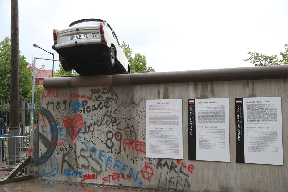 Součástí výstavy je i dochovaná část Berlínské zdi, přes kterou symbolicky letí trabant.