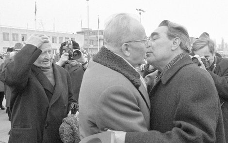 Brežněv polibkem zdraví Husáka na letišti před zasedáním států Varšavské smlouvy v Praze 24. ledna 1972, v pozadí přihlíží prezident Ludvík Svoboda.