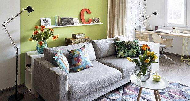 Obývací pokoj zútulňuje zelená barva na stěně a koberec s geometrickým vzorem.