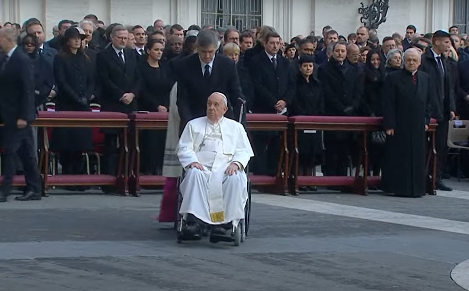 Papež František na vozíku, v pozadí česká delegace na mši za Benedikta XVI.