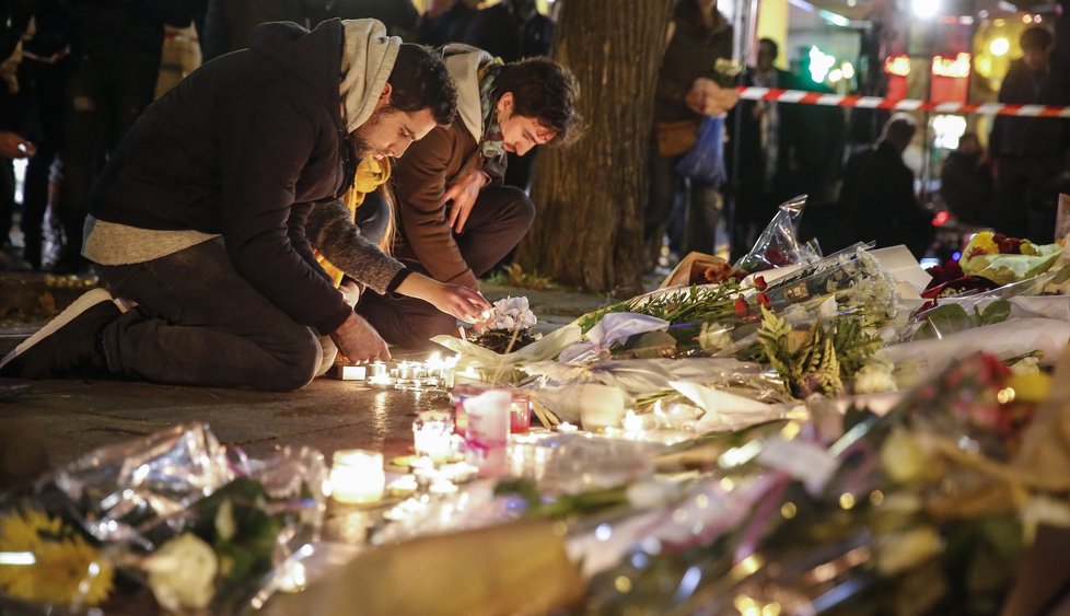 Lidé poblíž klubu Bataclan pokládají květiny a svíčky jako uctění obětí teroristických útoků 13. 11.