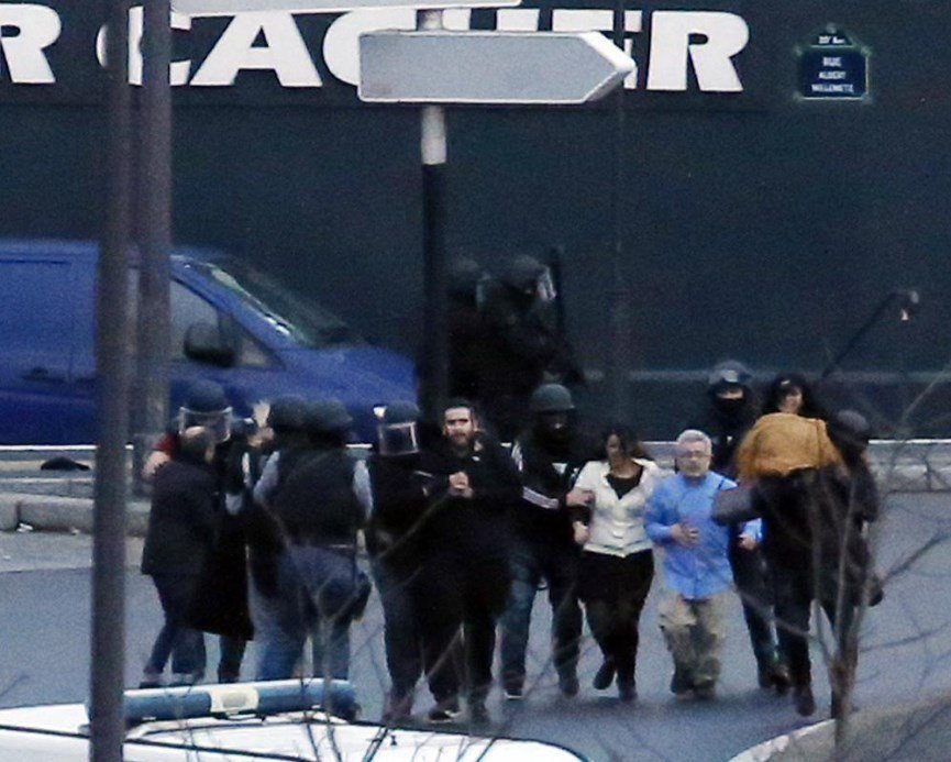 Policie vyvádí osvobozená rukojmí z košer obchodu, kde je držel terorista.
