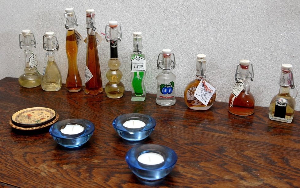 Na malé komodě jsou vyskládané láhve s pálenkami.