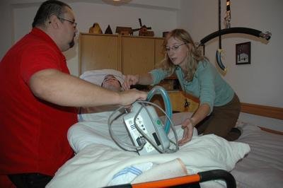 Saniťák spolu s ošetřovatelkou Hankou Křupalovou překládají Petra a dýchací přístoj na domácí postel
