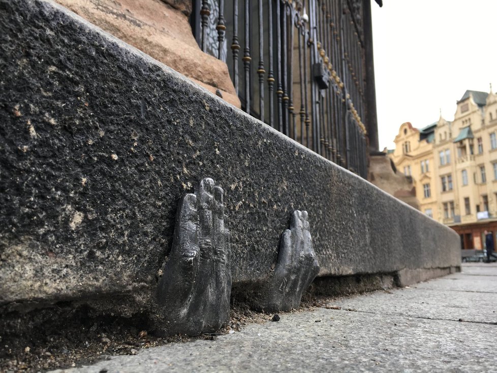 Kovová plastika rukou je na obrubníku katedrály sv. Bartoloměje u mříže s andílky.