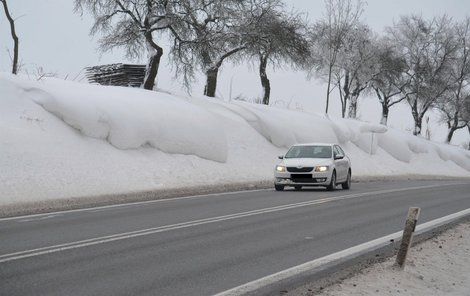 Závěje u obce Hosov se přelévají na silnici, zásněžky odpočívají složené za jedním ze stromů.